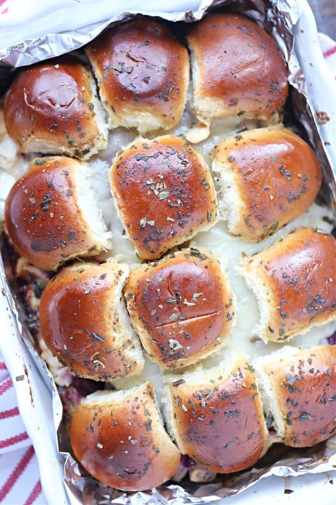 Overhead image of baked turkey cranberry sliders in a foil lined white baking dish.