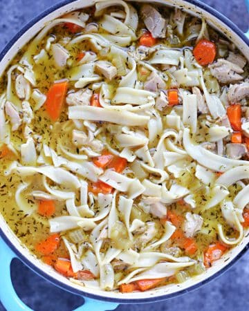 Overhead image of turkey soup in a blue and white dutch oven resting on a dark surface.