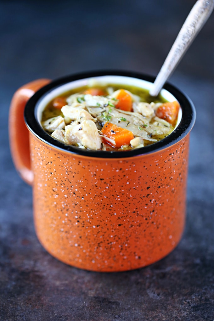 Turkey soup served in an orange mug with a spoon in it.