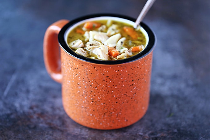 Turkey soup served in an orange mug with a spoon in it.