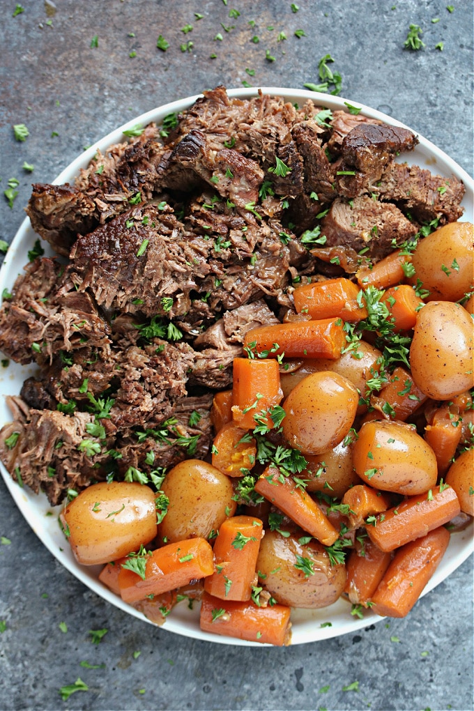 Overhead image of cooked pot roast and veggies on a white plate.